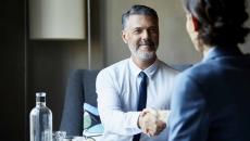 Two people sitting across from each other at a desk shaking hands