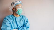 Healthcare worker in PPE stands with their arms crossed looking towards the side