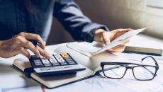 Person using calculator with pair of glasses and papers on table