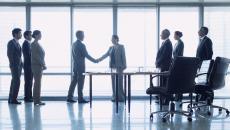 People standing in front of a window shaking hands while other people are watching