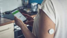 Person with a continuous glucose monitor checks their health data on a smartphone app