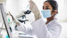 Researcher looking at a test tube and typing on a touchscreen computer