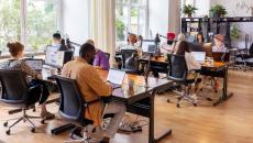 Numerous people sitting at large desks in a big room