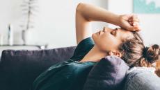 Person lying on a couch with their hand on their forehead with their eyes closed