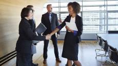 Four business people standing in a room with two of them shaking hands