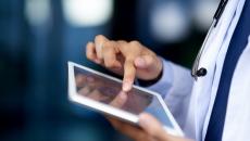 Healthcare provider using a tablet while wearing a white coat and stethoscope