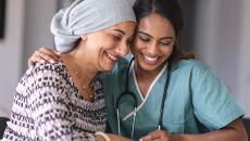 Two people sitting next to each other, one wearing a scarf on their head and the other in scrubs