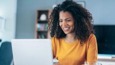 Person sitting at a table while looking at a computer and smiling