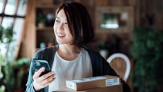 Person standing in their living room holding a phone and standing by stacked boxes