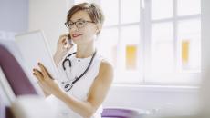 Healthcare provider sitting down in a clinicak setting while looking at a tablet 