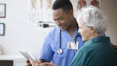 Healthcare provider standing in a clinic next to a patient while looking at a tablet