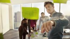 People standing in a board room looking at post it notes on a wall