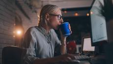 Person sitting at their computer drinking something out of a coffee cup