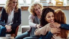 Group therapy session with four people in chairs, two of of them hugging