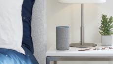 Light gray Amazon Alexa device on a bedside table next to a lamp, watch and houseplant