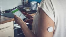 Patient with wearable glucose monitoring device looking at smart phone