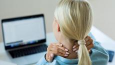 Person sitting at a desk with a laptop touching their neck