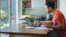 Person sitting at a table in a kitchen looking at their laptop