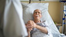 Senior patient holds the hand of a caregiver in hospital bed