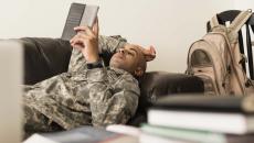 Soldier using digital tablet on sofa near books