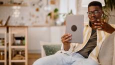 Person sitting on the couch in a home while holding up a tablet in front of them