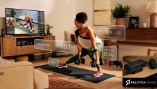 A woman lifting weights using the Peloton Guide while watching an instructor on her TV