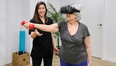 Person doing rehabilitation exercises while wearing a headset and standing next to a PT