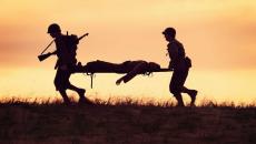 Two soldiers carrying another soldier on a gurney across a field