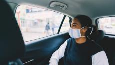 Person in a face mask sits in the back of a car looking out the window