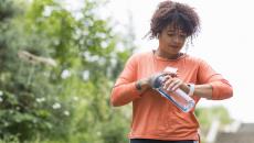 Person exercising checks their smartwatch while holding a water bottle and wearing wireless earbuds