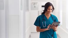 Healthcare provider wearing scrubs with a stethoscope around their neck while walking down the hallway of a health center