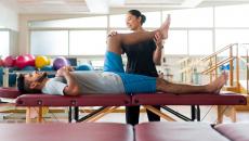 A male patient lying on his back on a massage table and a female physical therapist holding his leg up.