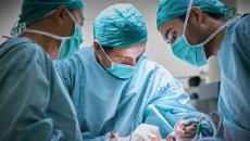 Three surgeons standing around a patient performing surgery in an operating room