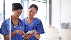 Two healthcare providers wearing blue scrubs and looking at a tablet