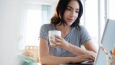 Person sitting at a computer while holding a coffee cup