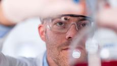 Scientist in a laboratory wearing safety goggles and putting something in a beaker