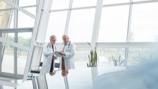 Two healthcare professionals standing in a large room with windows