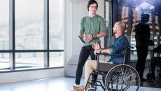 Two people in a room next to a lot of windows with one in a wheelchair