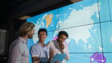 Three people standing in front of a large board showing the world map