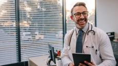 Doctor leaning against a desk while holding a tablet 