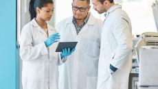 Three healthcare professionals standing in a circle looking at a tablet