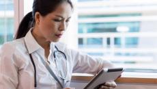 Person sitting by a window wearing a stethoscope and looking at a tablet