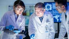 Three healthcare professionals in lab coats looking at something under a light