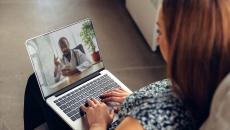 Person sitting on their couch with a computer on their lap talking to a virtual healthcare provider