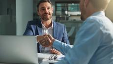 Two people sitting on opposite sides of a desk and shaking hands