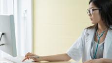 A doctor reviewing a patient's record in a desktop computer