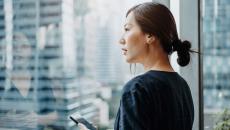 A person holding a smartphone looking out a window. 