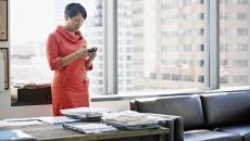 Businesswoman standing in office looking at smart phone smiling