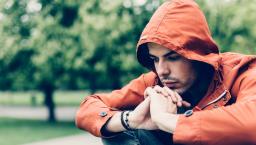 Person sitting in a park while wearing an orange sweater with a hood