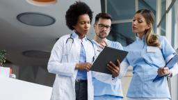 Three healthcare providers standing next to each other and looking at a tablet